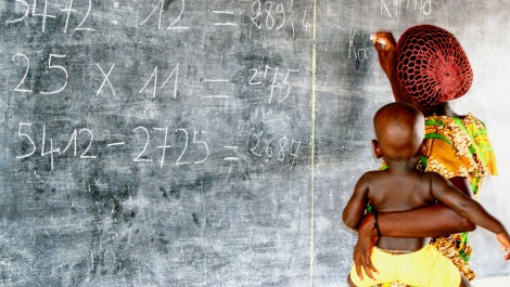 Африканка пише на черна дъска, носейки малко дете на ръце © ЕС