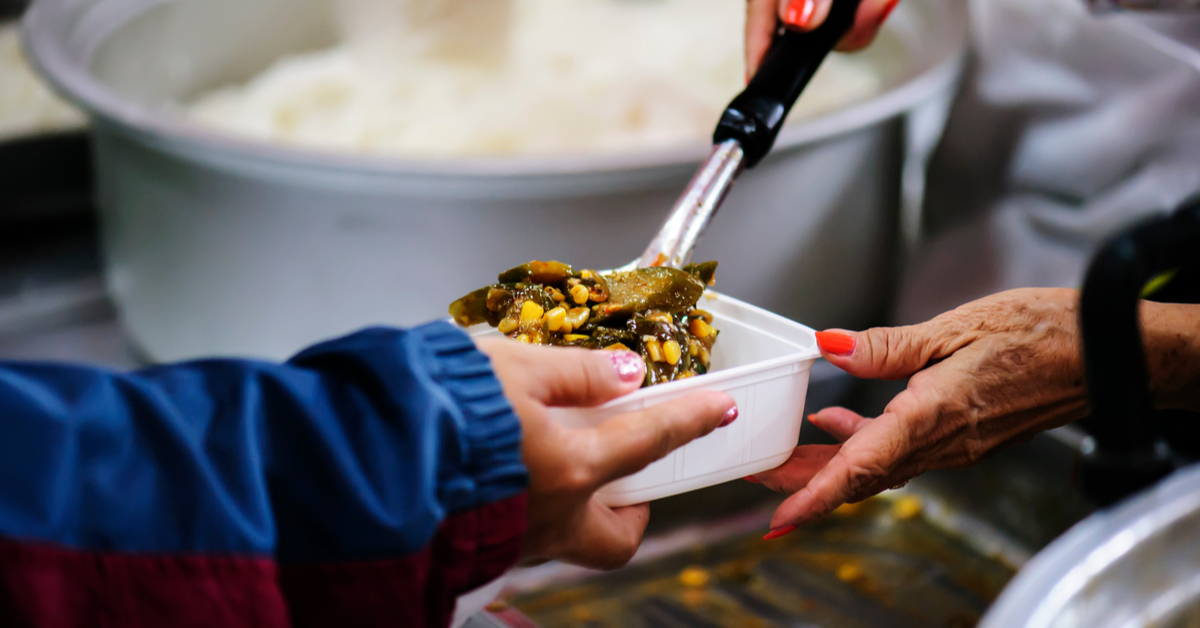 Hands of two persons in a charity canteen: one is holding a Tupperware while the other is filling it with food 