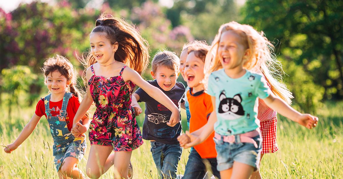 Group of happy young children running on a sunny day in a grass field