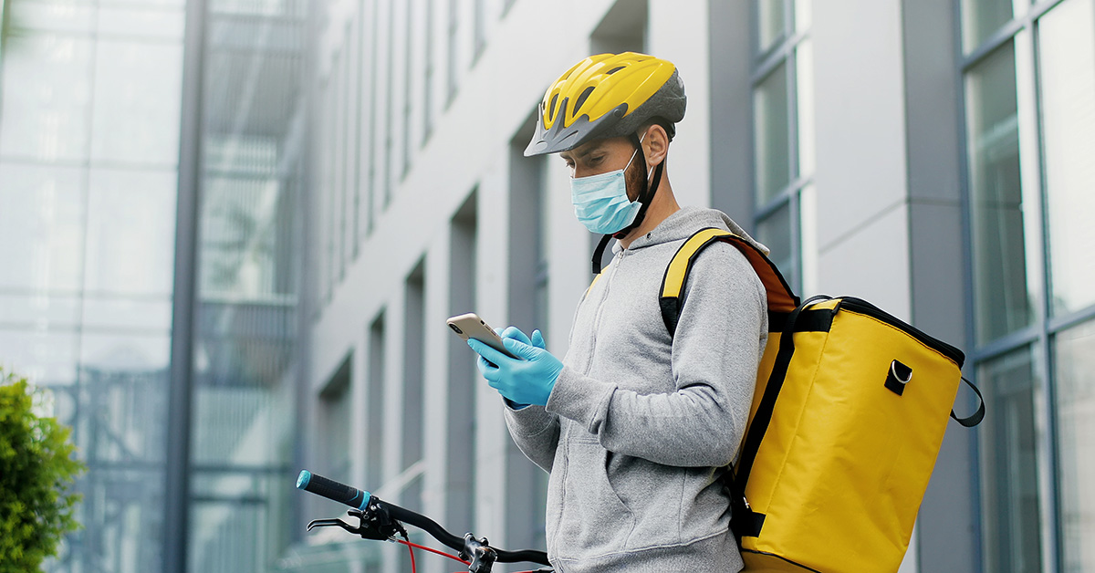 Portrait of male courier in medical mask and helmet for riding bike on bicycle delivering food.