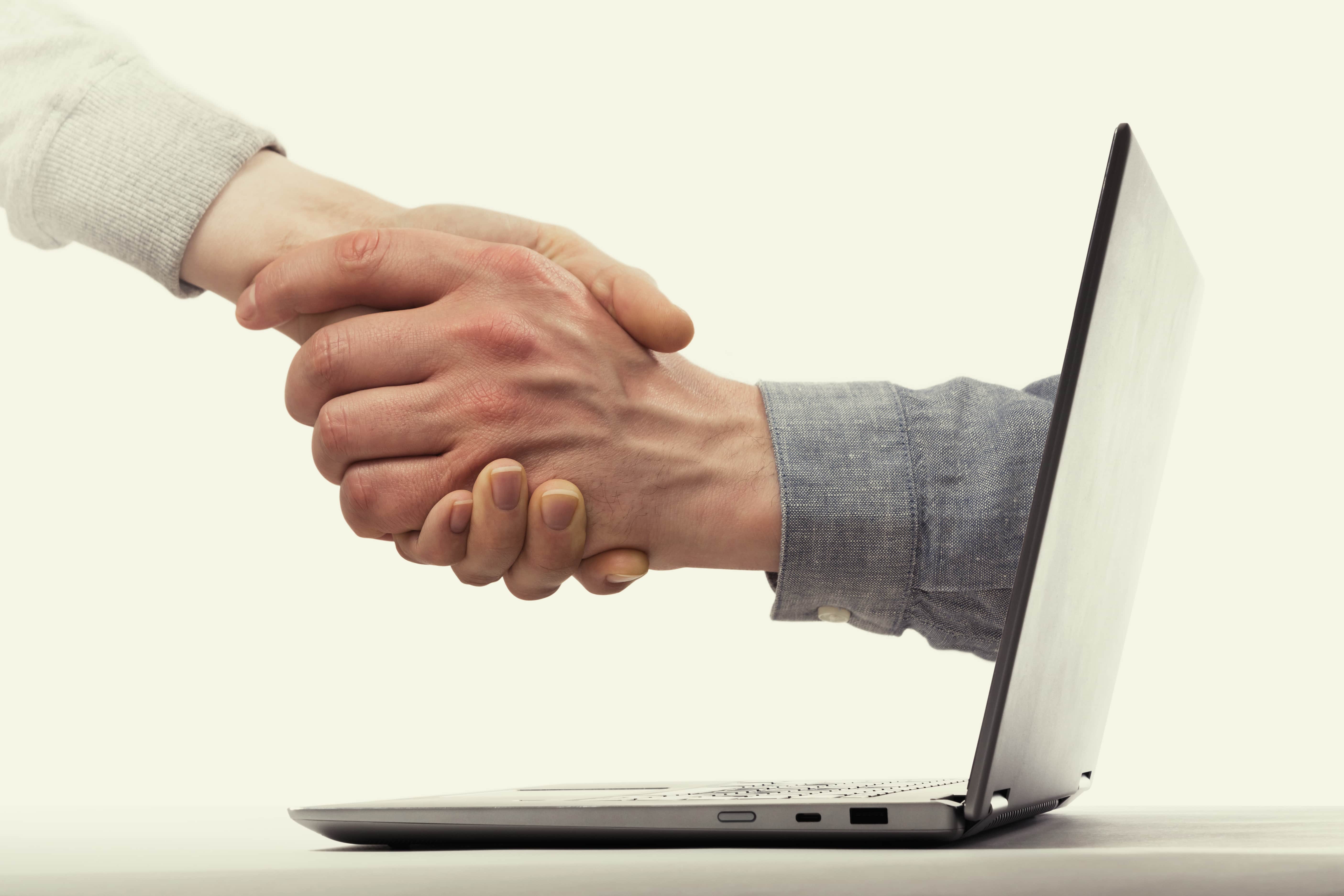 A hand emerging from a computer screen shaking another hand