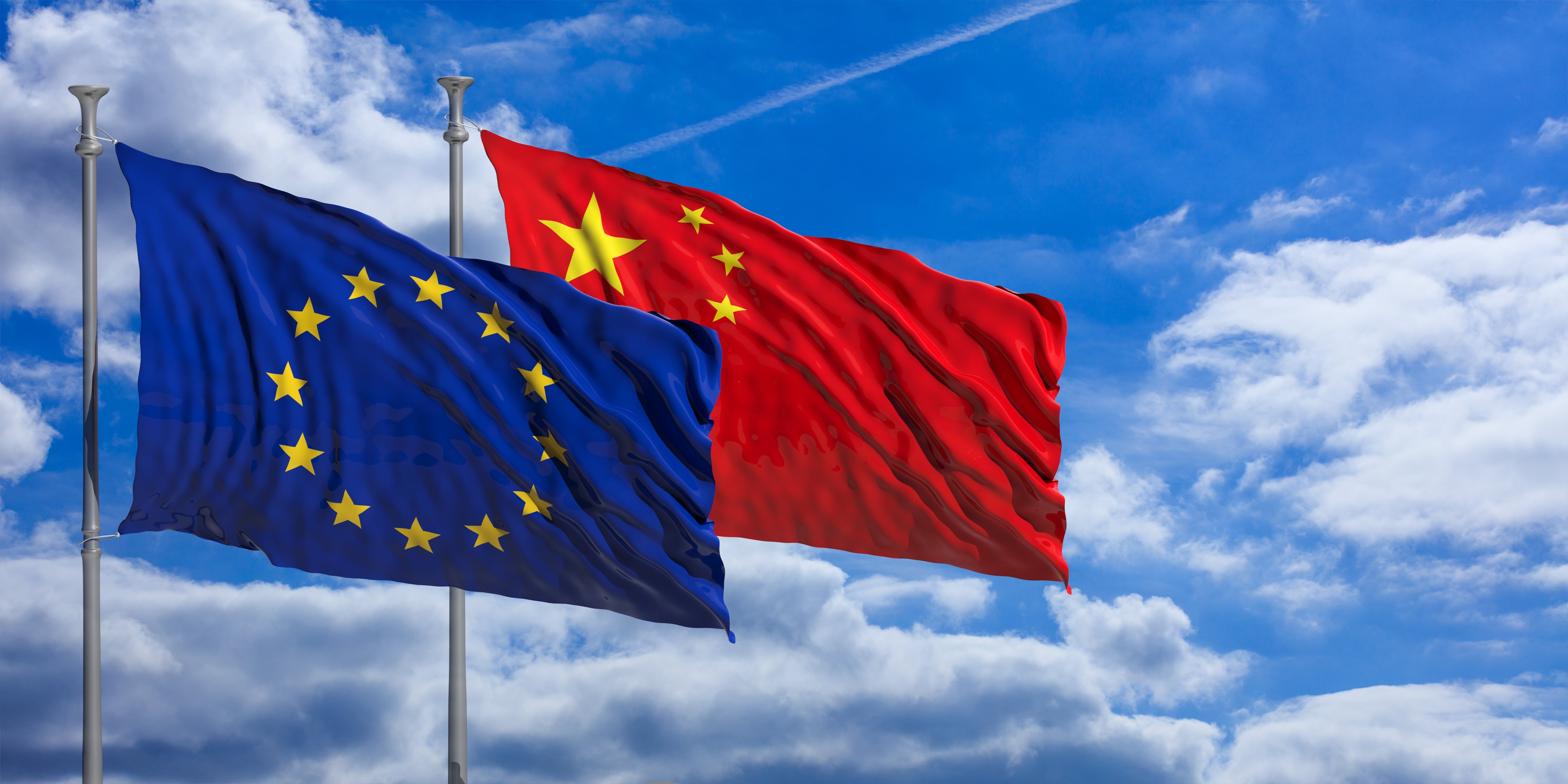 An EU flag and a Chinese flag flapping next to each other in the wind against a light blue sky with white fluffy clouds