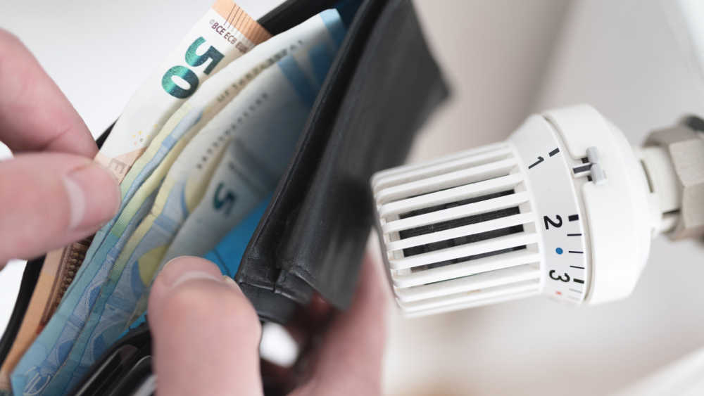 A thermostat of a radiator and a person standing with an open wallet with euro notes in it