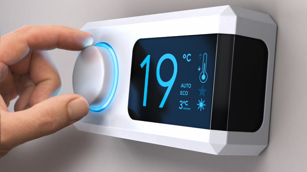 Hand turning a home thermostat knob to set temperature on energy saving mode