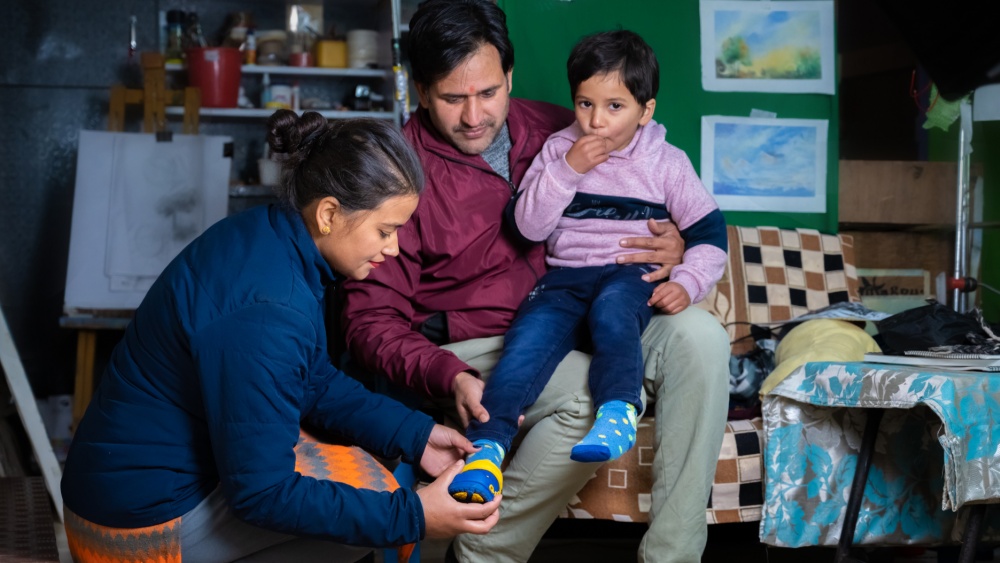 Child sitting on a man's lap while a woman puts on his shoe.