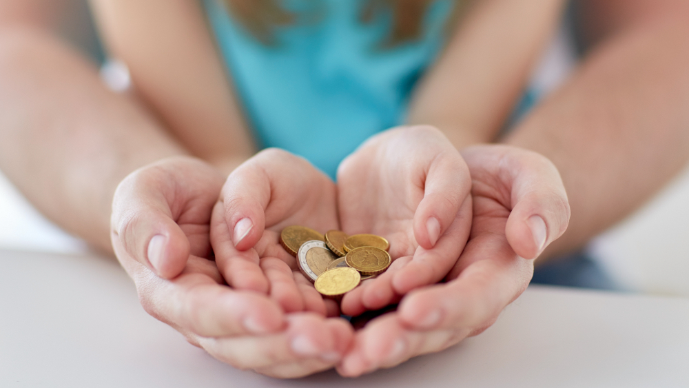 A mother having her hands under a child´s hands, while the child is holding money in it´s hands.