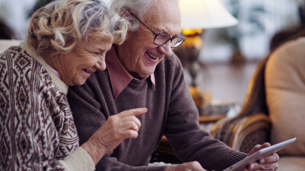 Two older people looking at a tablet and smiling.