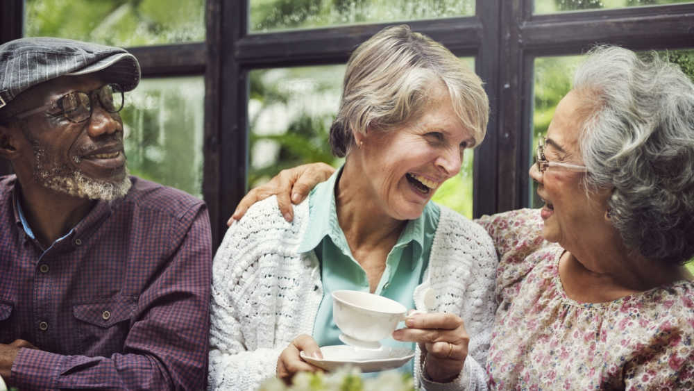 3 older people sharing a lough while drinking tea.