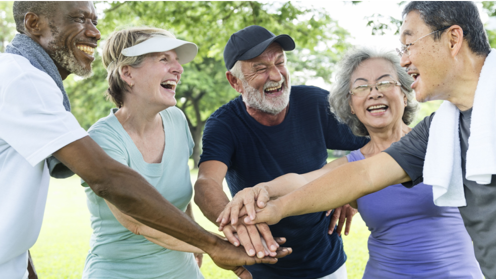 A group of older people laughing and placing their hands on top of each other's