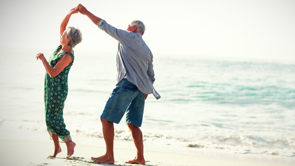 Two aging people are dancing on a beach
