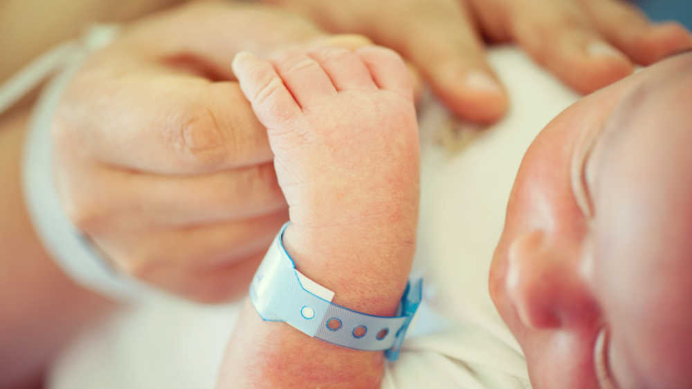 An adult holds the hand of a newborn child