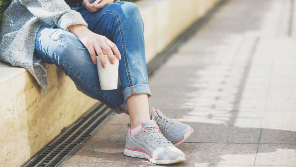 A woman is sitting on wall with a cup in her hand. Only the lower part of the woman can be seen.