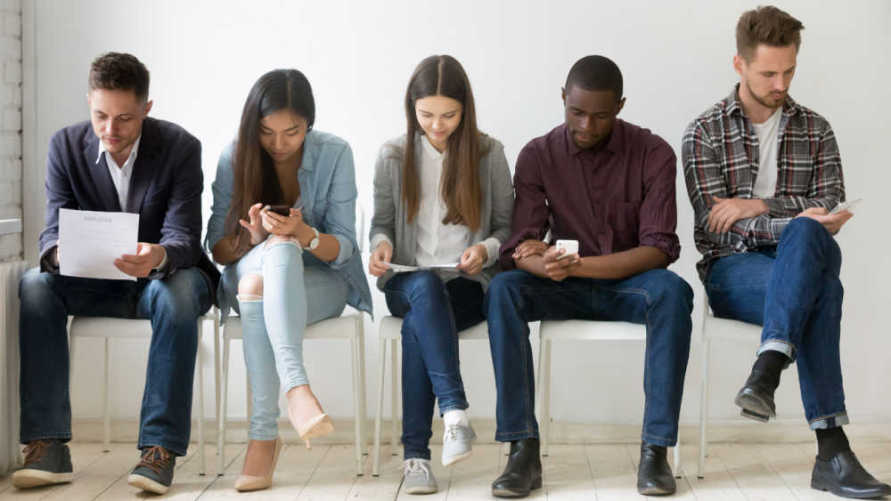 Four young people in a waiting room, looking at their phones and papers.