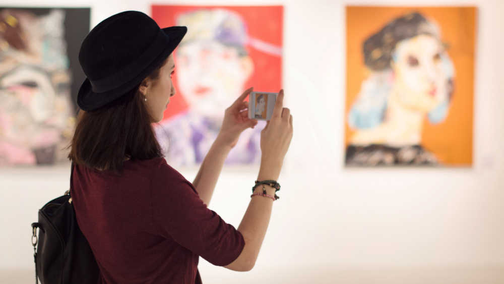 A woman photographing some paintings in a museum