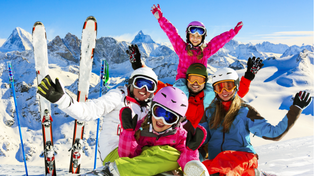 Two adults and three children taking a family photo in skiing gear on the mountain