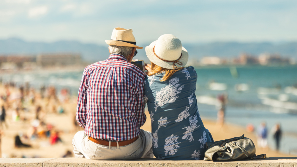 Two older people siting at the beach looking at the sea