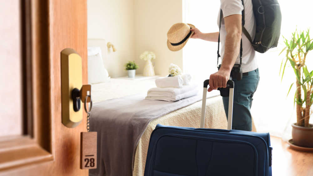 A person holding a hat and a briefcase entering a hotel room.