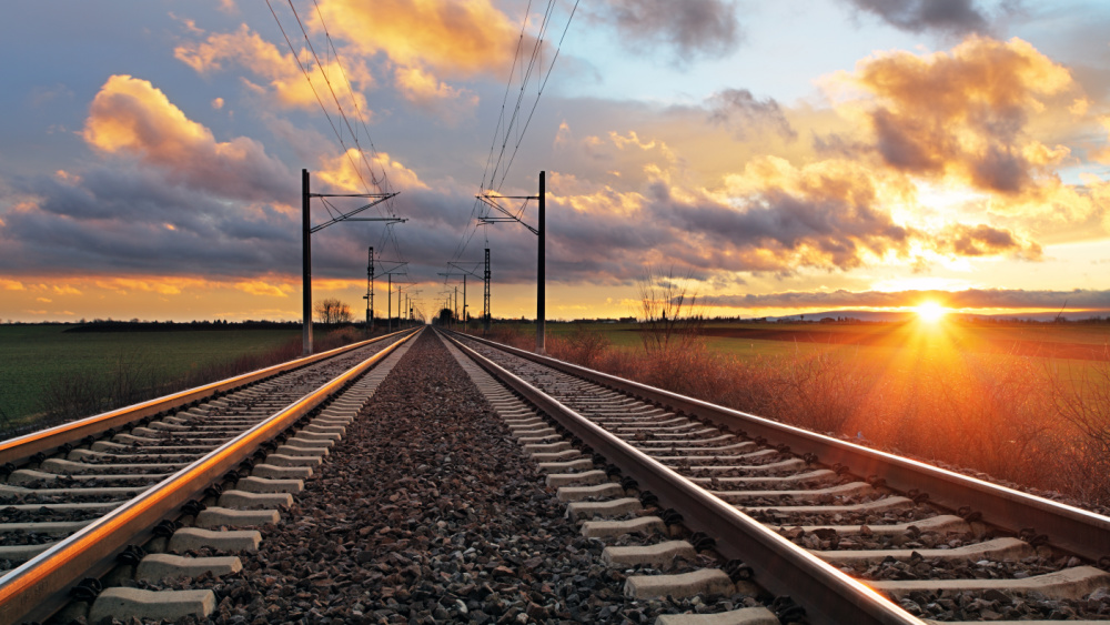 A railway track with fields around and a sunset in the background