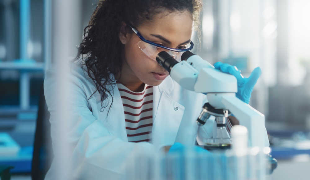 Young woman sitting in a laboratory in front of a microscope and looking into it