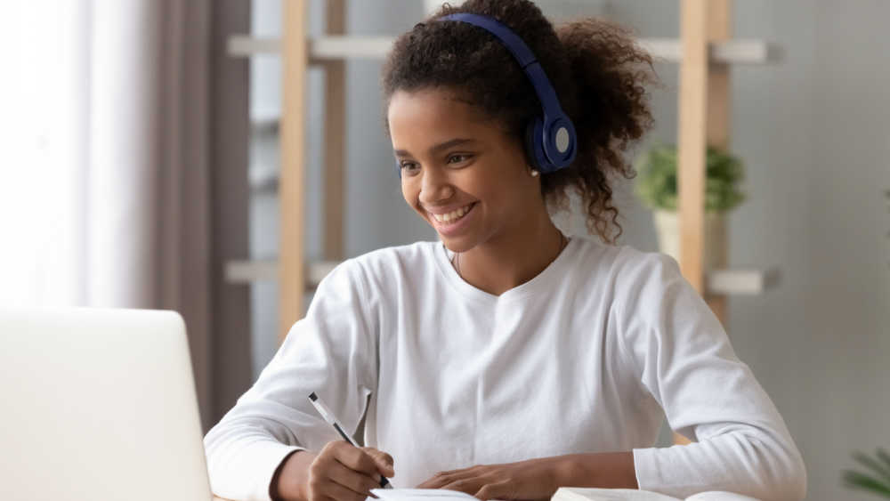 Smiling teenage girl wearing headphones using laptop