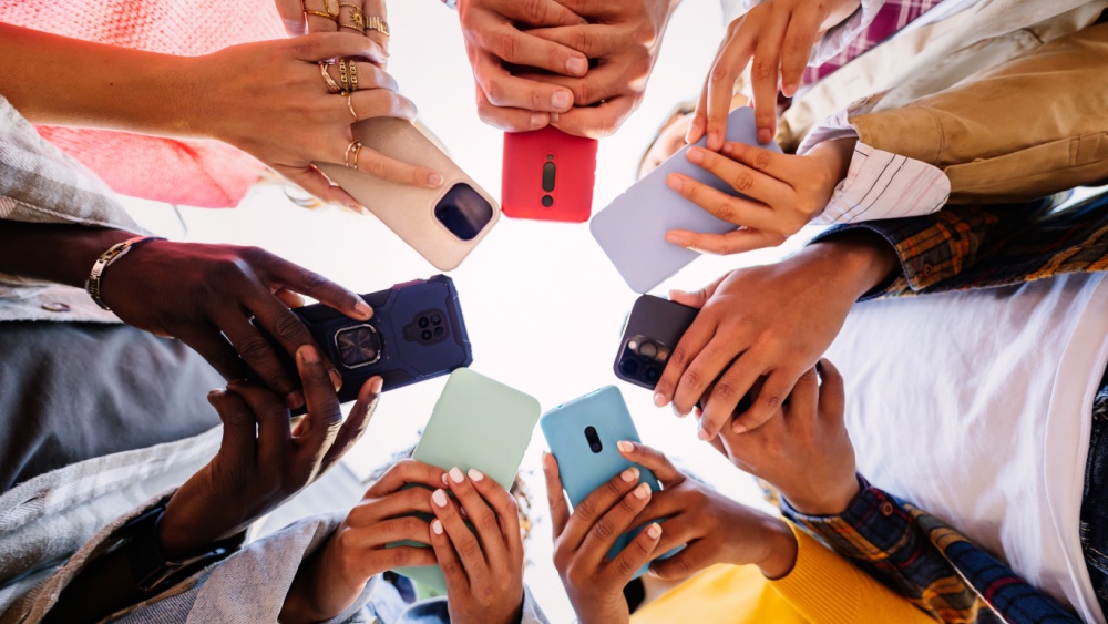 Seven people are standing with their mobile phones in their hands, forming a circle and can be seen from below and up