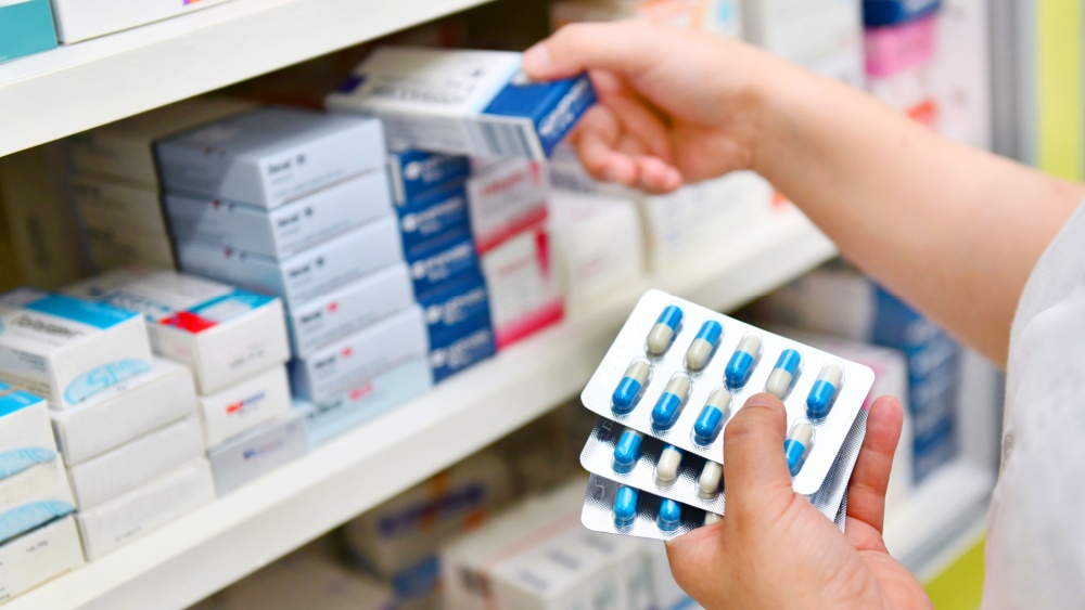 A person picking medicines of the shelf in a store.