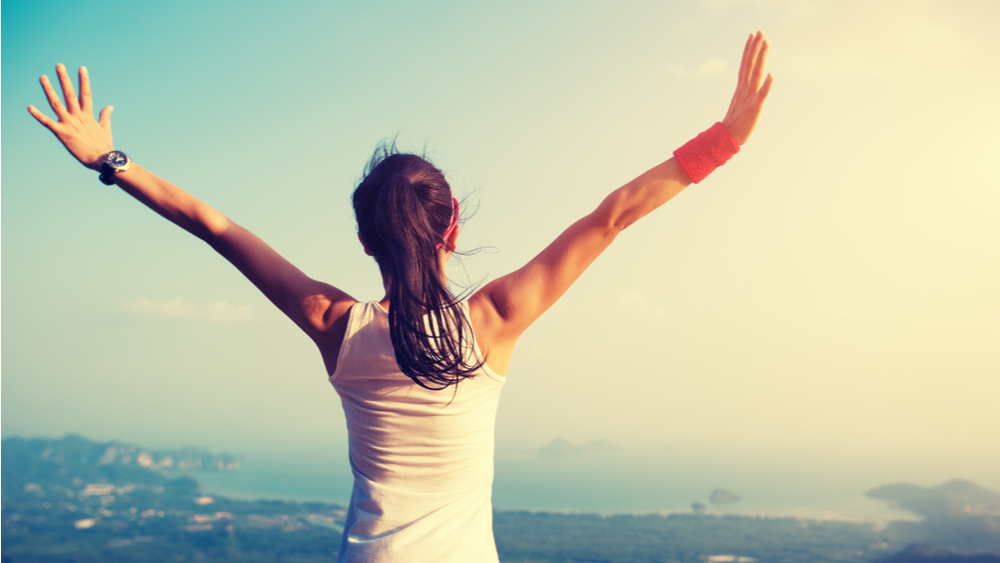 Young woman raising arms at mountain peak cliff