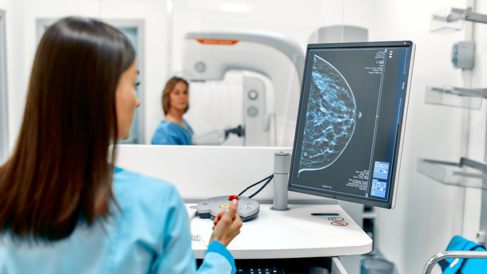 A room is equipped with a mammography unit and a doctor is scanning a woman´s breast