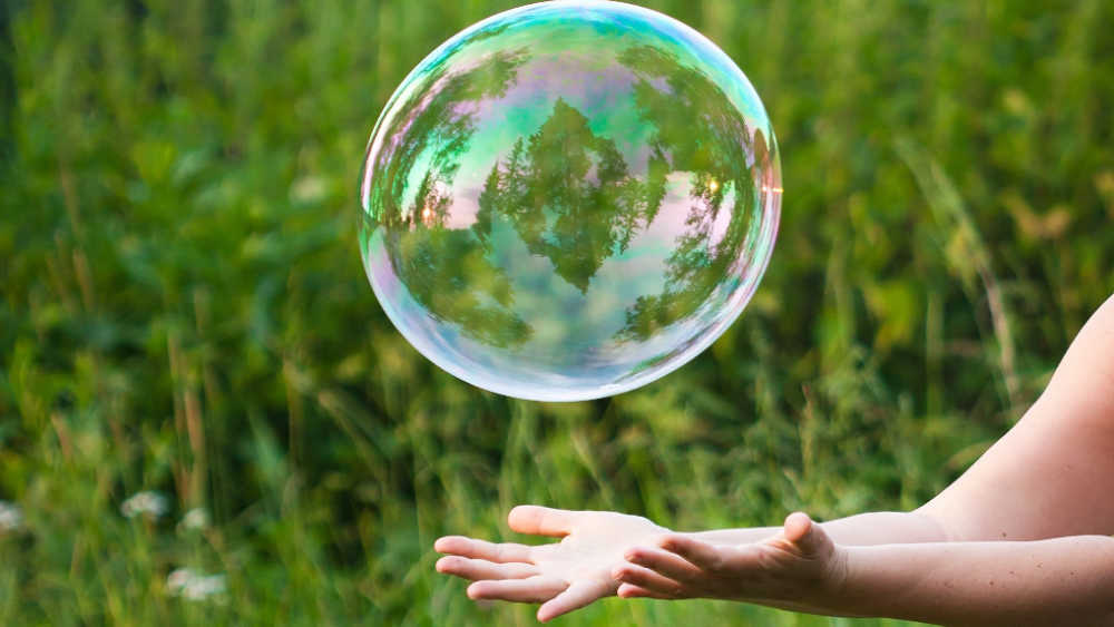 child hands hold big bubble in a green field