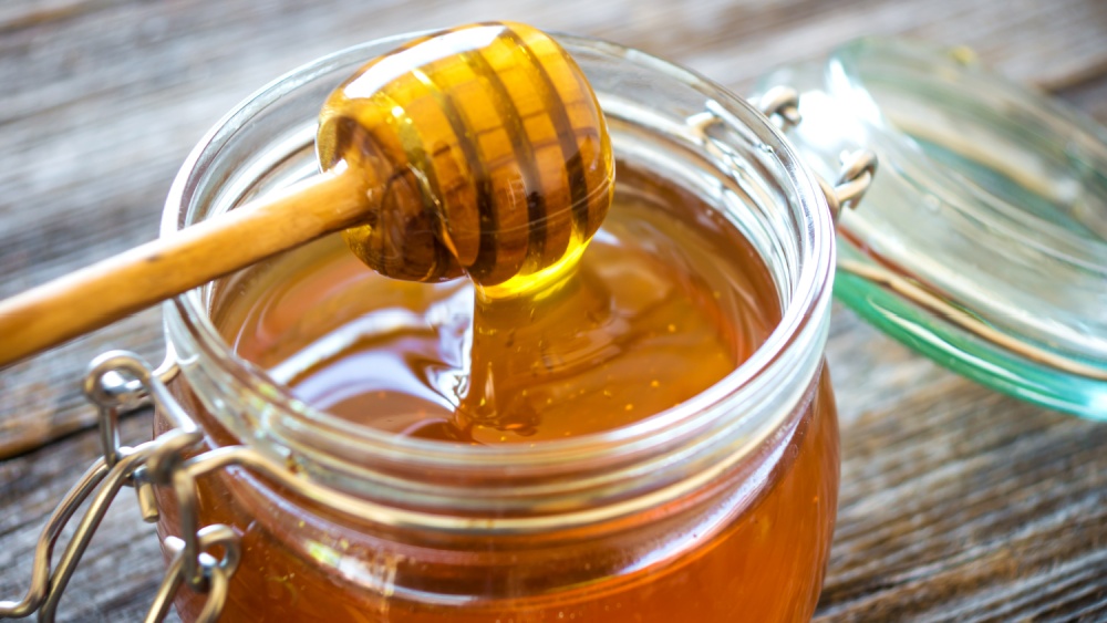 A jar with honey is open and a honey spoon is filled with honey