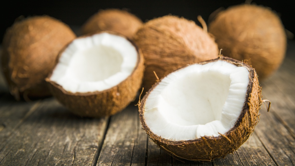 Five coconuts on a wooden table, one is split open.