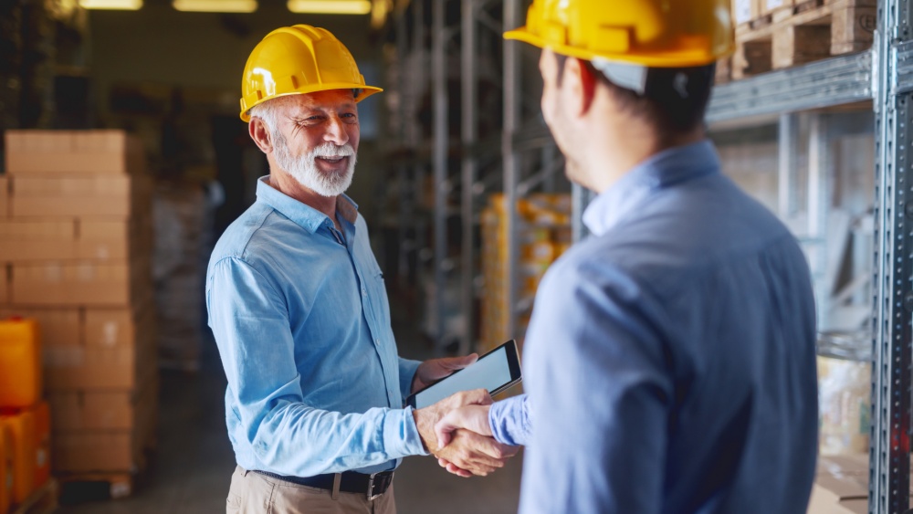 Two men with safety helmets on shake hands.