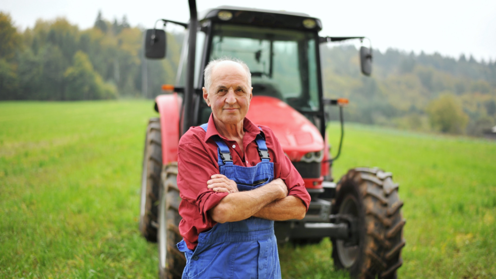 A person wearing overalls standing with arms crossed in front of a tractor.