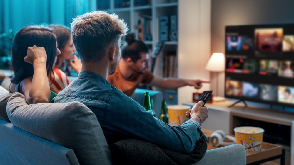 A group of people sitting on the couch picking what to watch from a streaming service on TV.