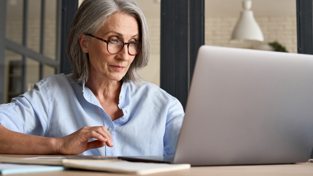 A women with grey hair writing on a laptop.