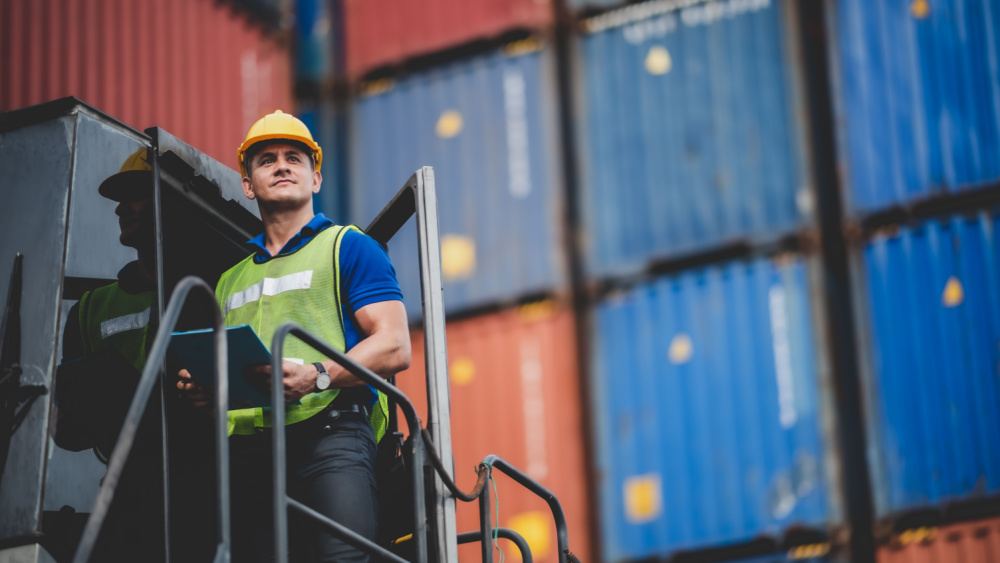 man wearing a yellow vest standing in the container platform looking ahead