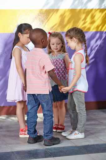 Photograph of four children, three girls and one boy of different ethnicities standing and holding hands in circle.