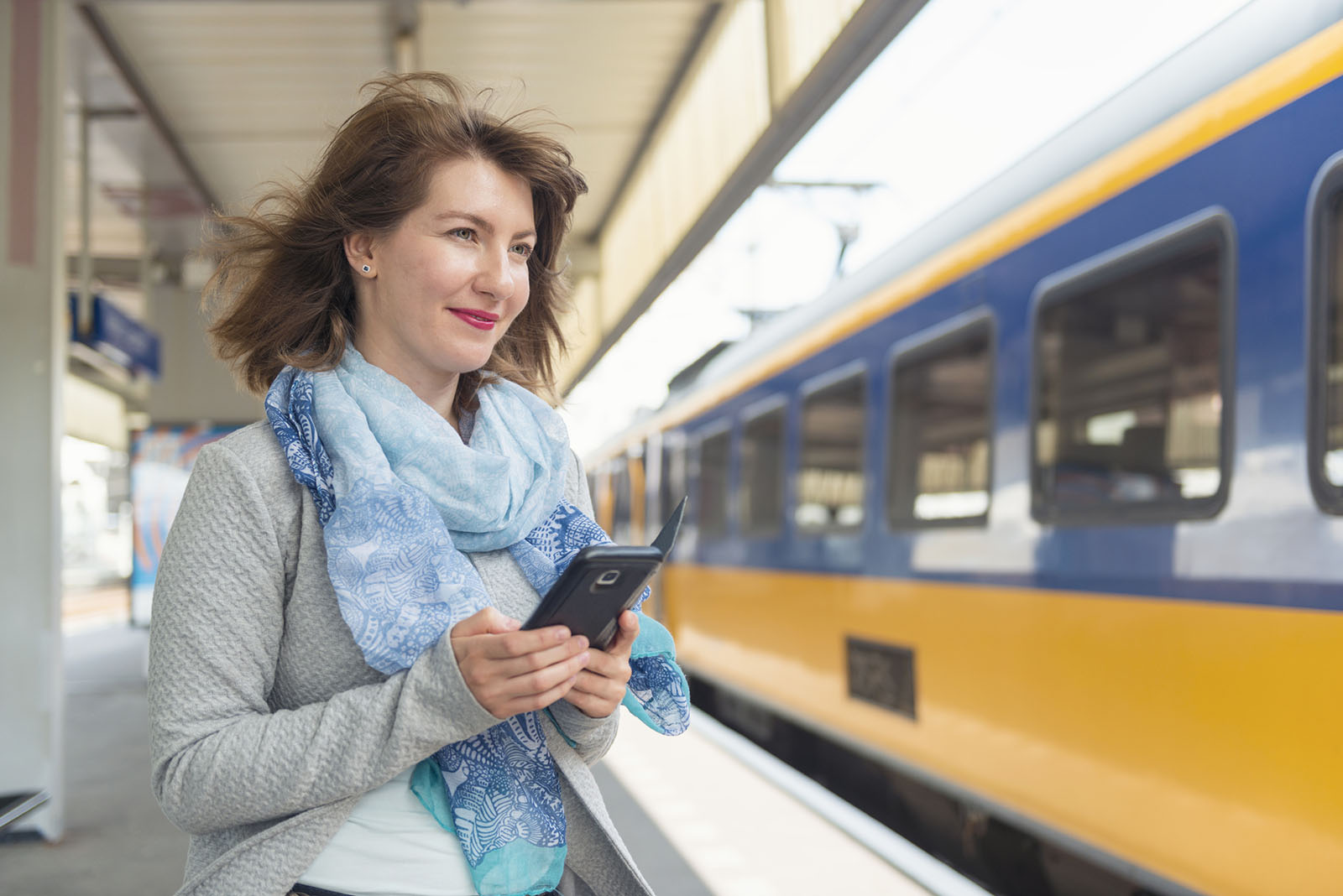 nainen seisoo junalaiturilla matkapuhelimella
