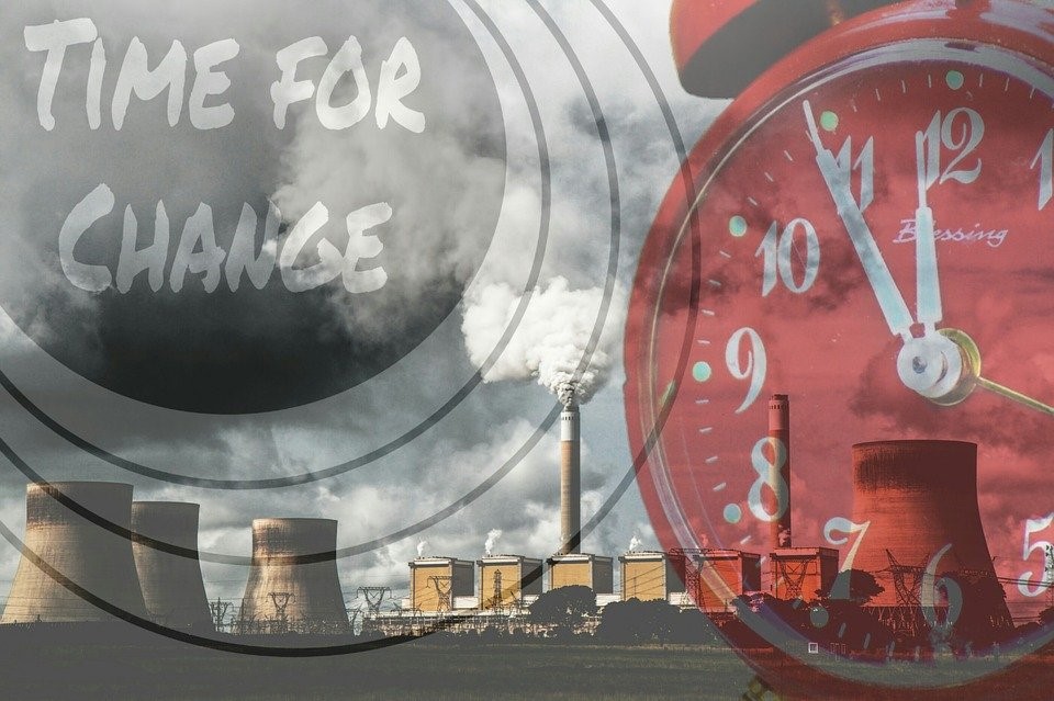 Time for change - power plant in background, red alarm clock showing 5 minutes to 12