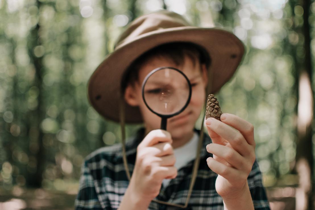A boy examines a nature sample in his hands with a magnifying glass