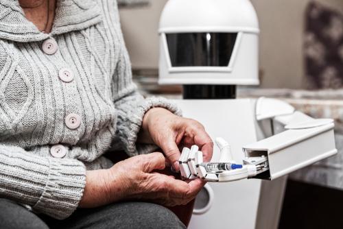 Autonomous caregiver robot is holding an insulin syringe, giving it to a senior adult woman in her living room. © Miriam Doerr Martin Frommherz, Shutterstock
