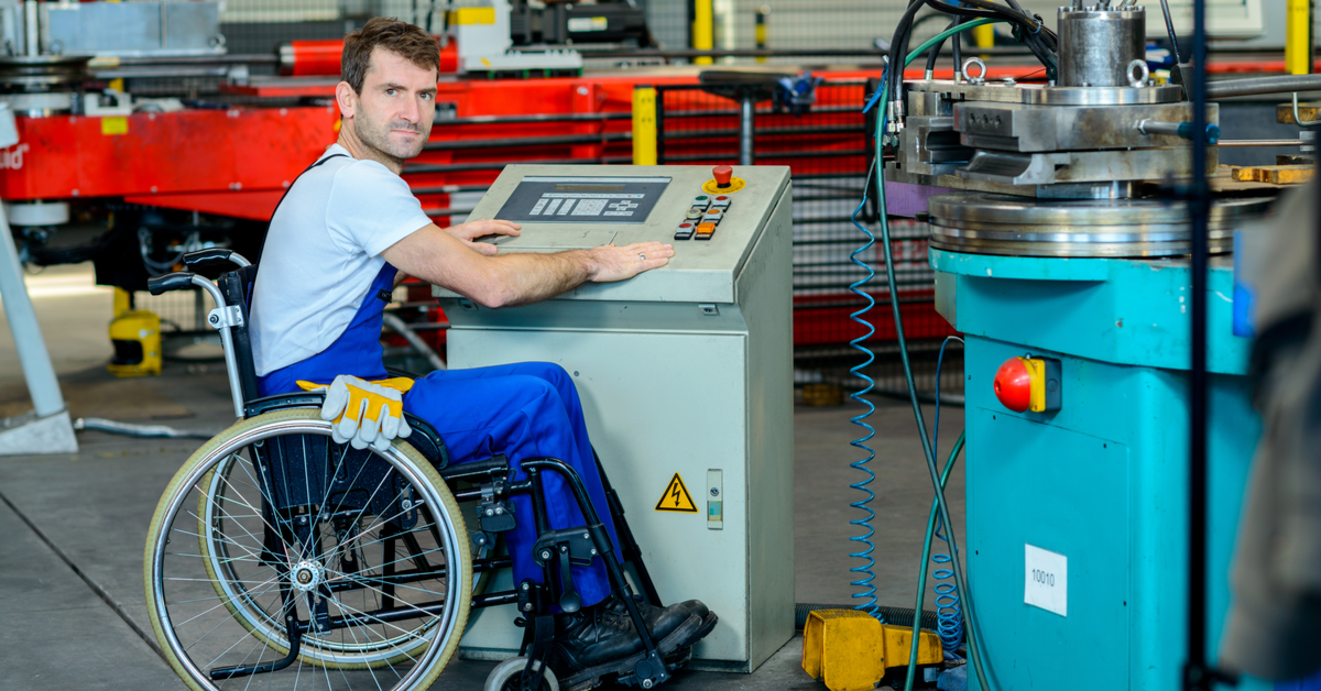 Disabled worker on a wheelchair in a factory  in front of a machine
