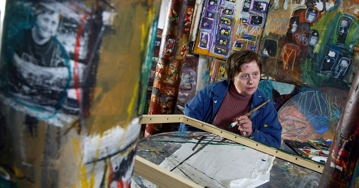 Femme, présentant une trisomie 21, qui peint une table dans un atelier de peinture