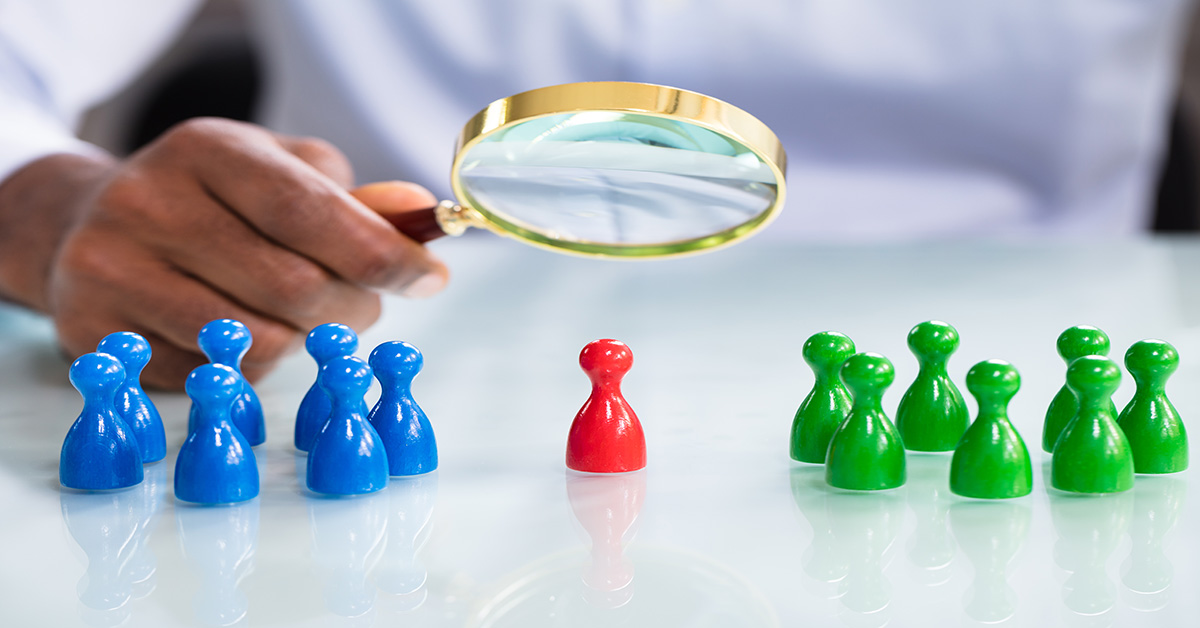 A man looking at colourful pawns with magnifying glass on the reflective desk