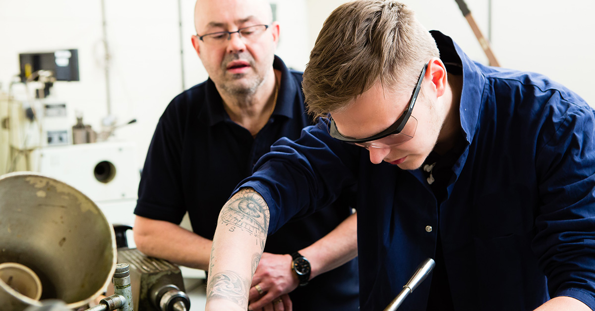 An apprentice in a workshop receiving training advice from a senior employee