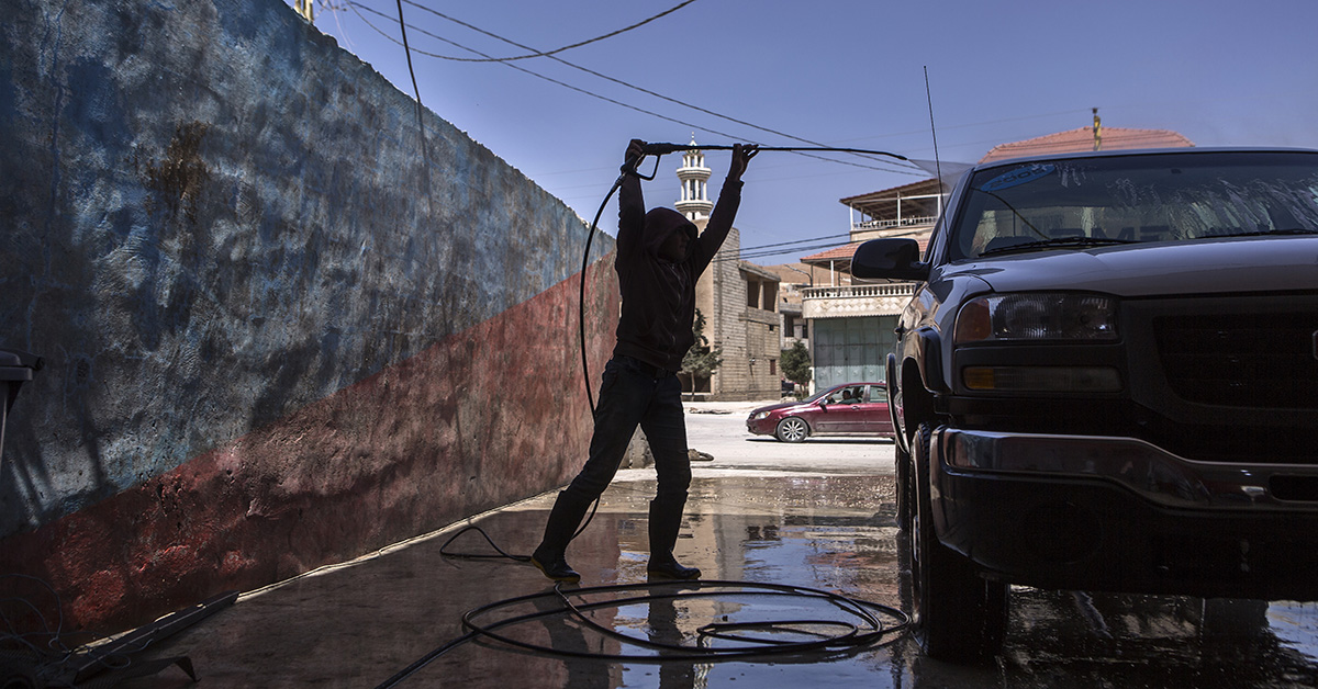 Young boy washing a car with a hose