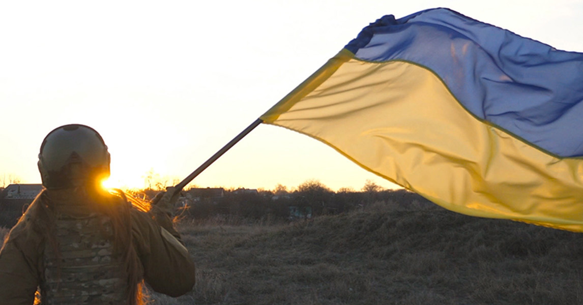 Soldier moving a Ukrainian flag in front of rising sun