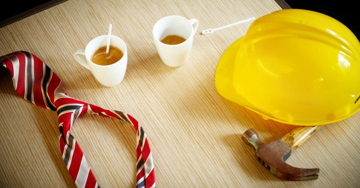A tie, a safety helmet, a hammer and two cups of coffee on a table