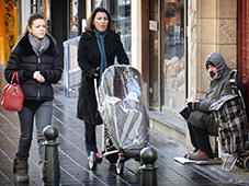 Aman begging on the street and two women with a stroller passing by