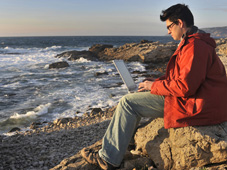 Mann, der am Computer arbeitet und am Strand sitzt.